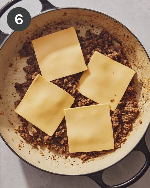 Cheese slices topping ground beef in a skillet.
