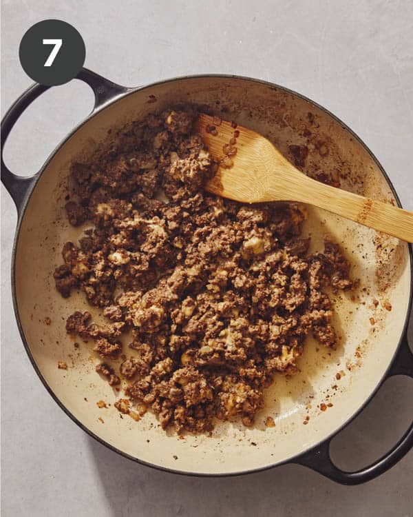 Cheese mixed with ground beef in a skillet to make a chopped cheese sandwich.