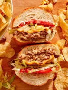 A chopped cheese sandwich cut in half on a cutting board.