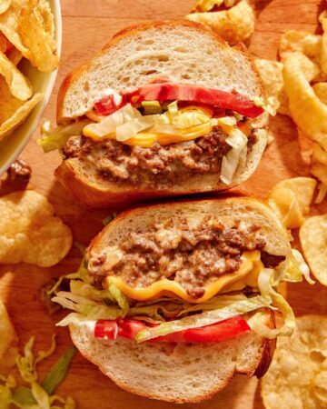 A chopped cheese sandwich cut in half on a cutting board.