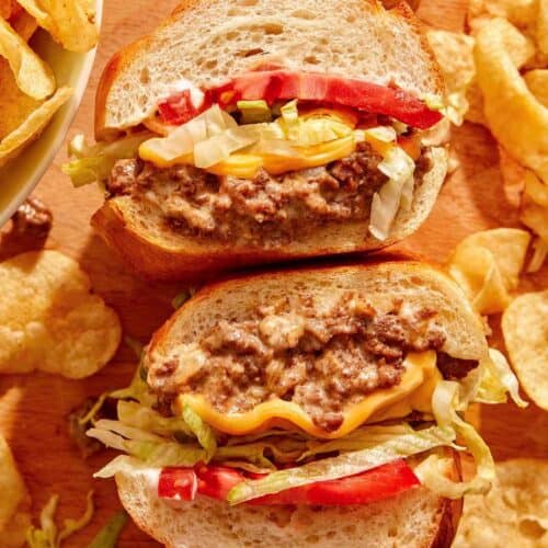A chopped cheese sandwich cut in half on a cutting board.