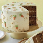 Layered carrot cake on a pedestal with a slice out.