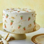 Carrot cake on a cake stand with plates next to it.