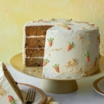 A carrot cake on a cake stand with a slice out sitting next to it.