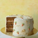 A carrot cake on a cake stand with a slice out to see layers.