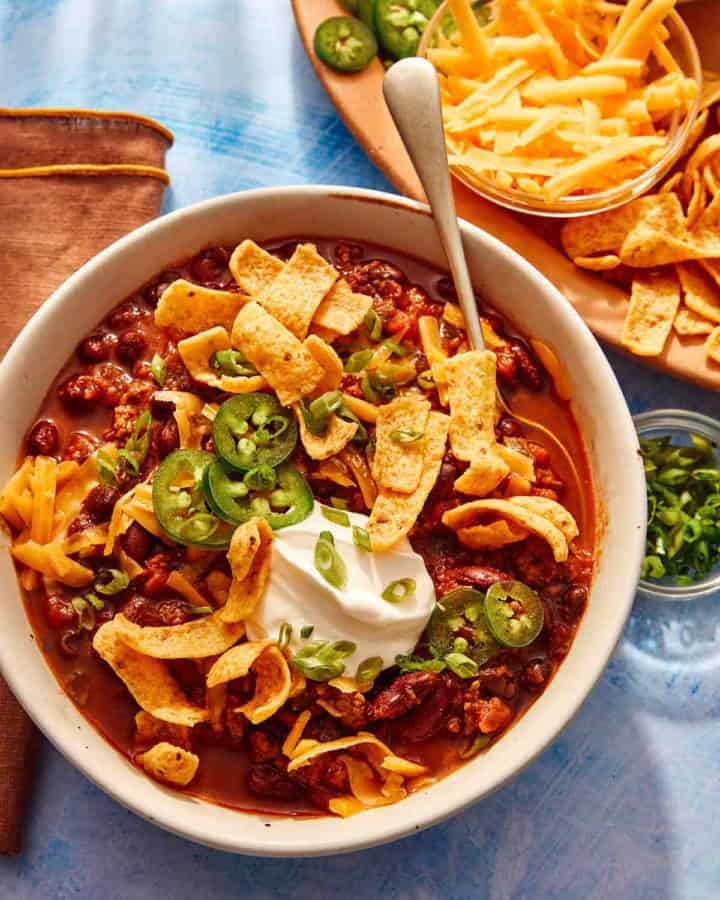 Chili being served in a bowl with toppings on the side.
