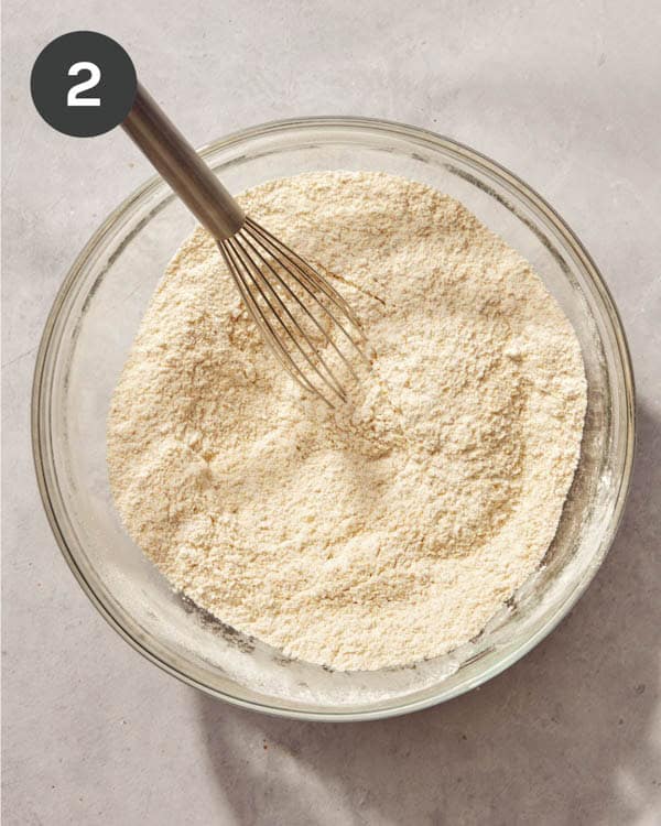 A glass bowl filled with cornmeal and flour being whisked together.