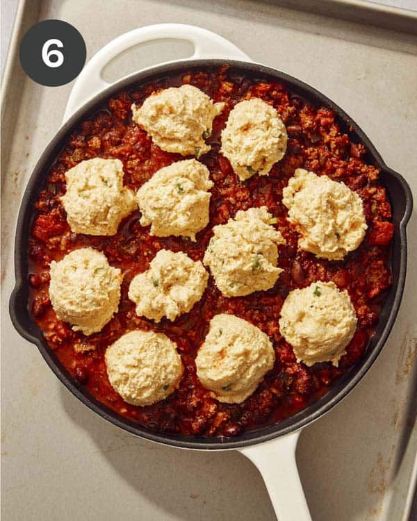 Dollops of cornbread dough over top chili in a skillet.