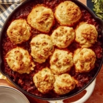 Chili cornbread casserole in a skillet with bowls next to it.