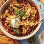 Chili in a bowl with a spoon in it and toppings on the side.