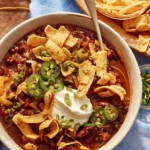 Chili being served in a bowl with toppings on the side.