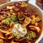 A chili recipe in a bowl with a person taking a bite out of a it with a spoon.