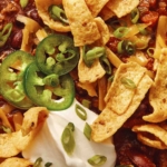 A close up shot of chili in a bowl with toppings and a spoon.