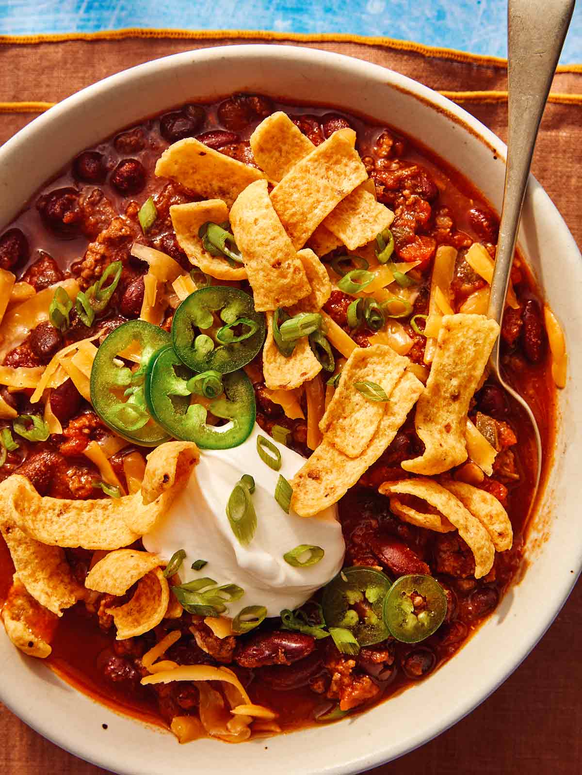 A close up shot of chili in a bowl with toppings and a spoon.