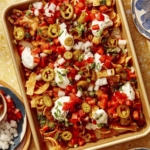 Frito pie on a baking sheet with plates of frito pie around it.