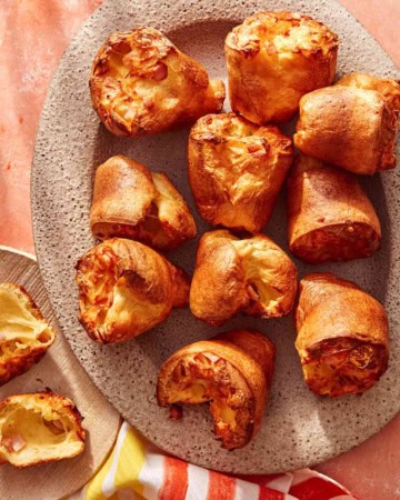 Popovers being served on a platter with a plate next to it with a popover ripped open.