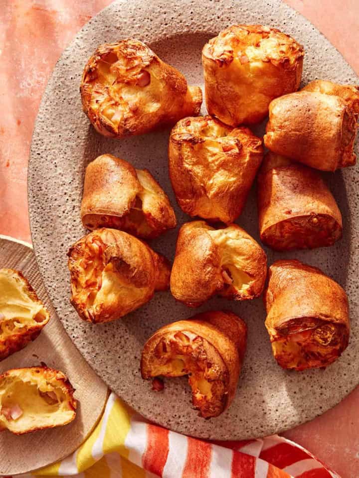 Popovers being served on a platter with a plate next to it with a popover ripped open.
