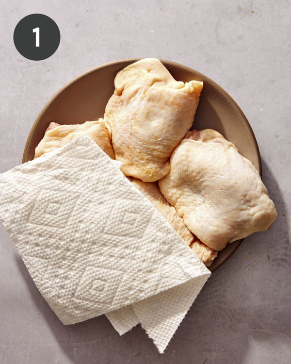 Chicken thighs being dried off with a paper towel on a plate.