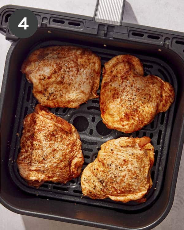 Chicken thighs ready to be cooked in a basket of an air fryer.
