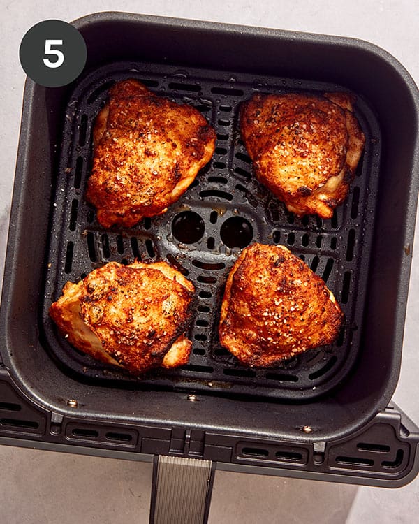Chicken thighs cooked in an air fryer basket.
