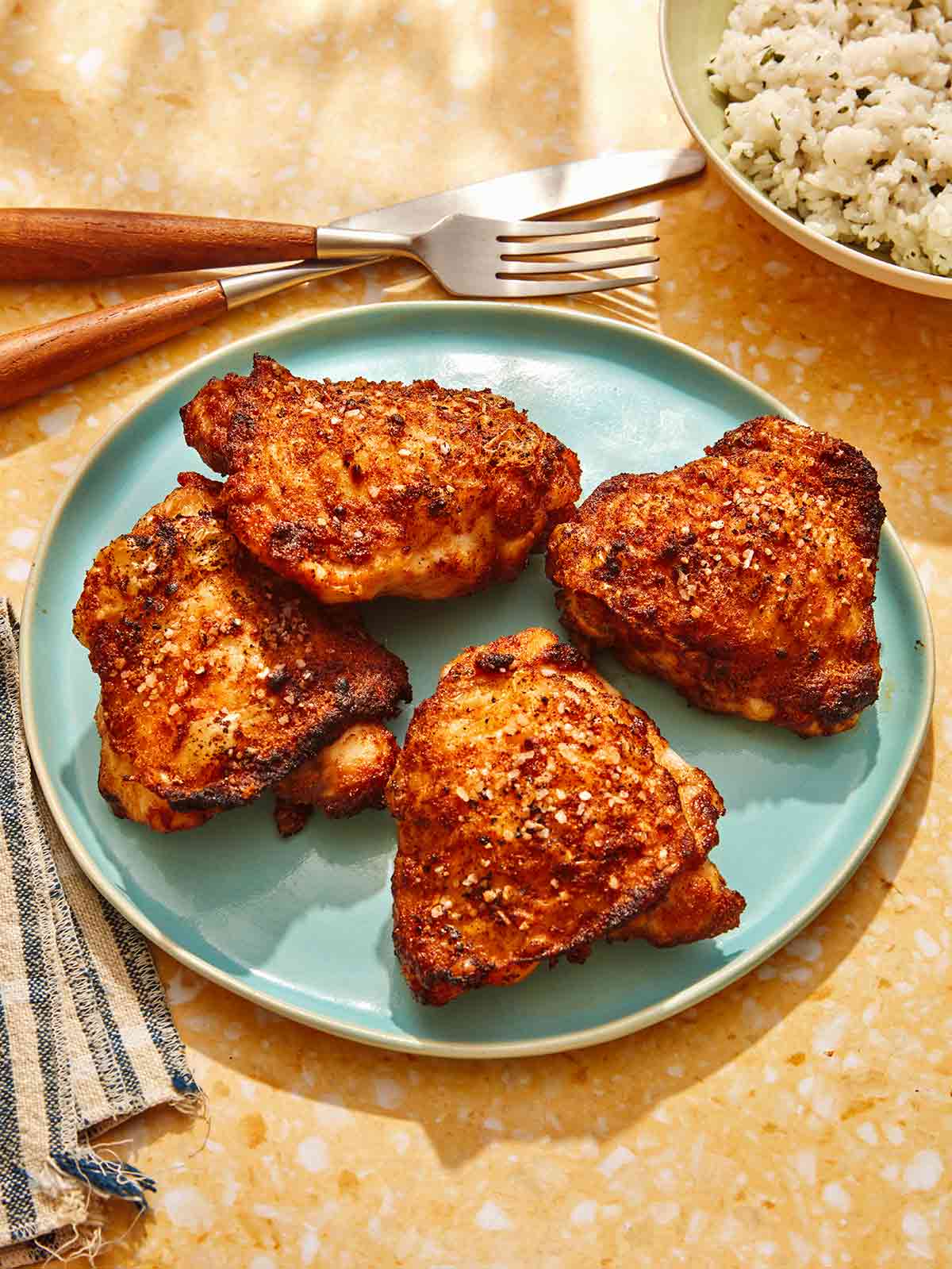 Seasoned chicken thighs on a plate with rice in the background.