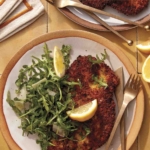 Chicken milanese recipe on two plate with forks and knives.