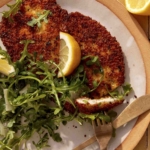 Chicken milanese being cut into on a plate.