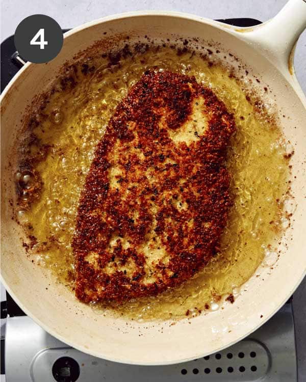 A breaded chicken breast being friend in a pan.