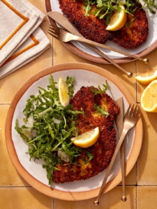 Chicken milanese recipe on two plate with forks and knives.