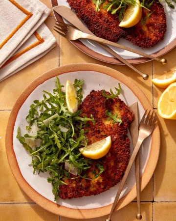 Chicken milanese recipe on two plate with forks and knives.