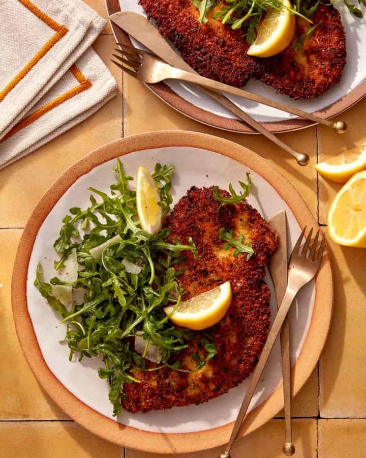 Chicken milanese recipe on two plate with forks and knives.
