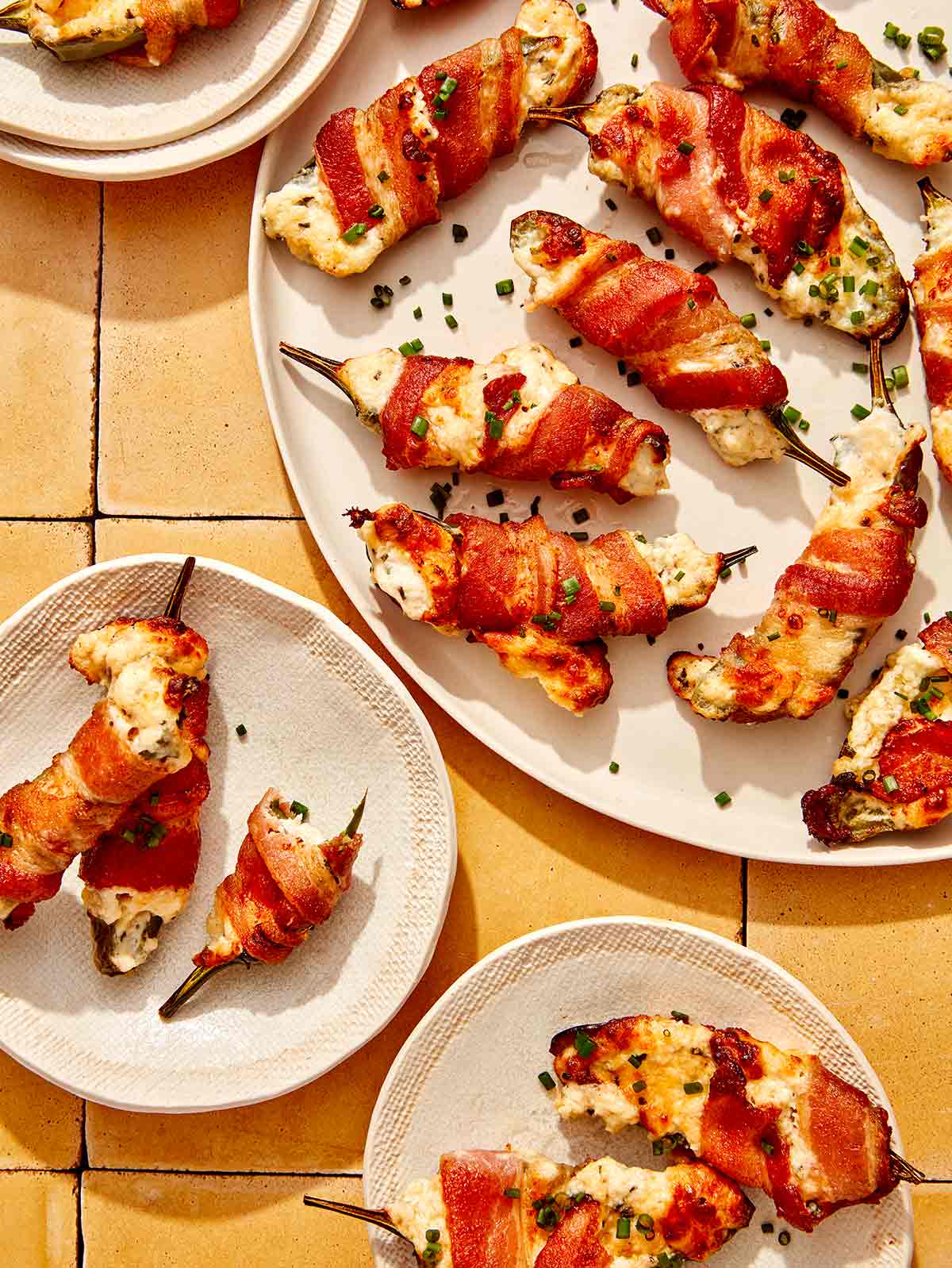 Bacon wrapped jalapeno poppers on a platter with some being served onto plates.