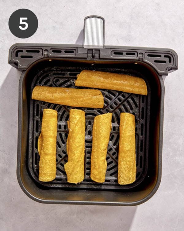 Taquitos lined up in an air fryer.