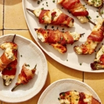 Bacon wrapped jalapeno poppers on a platter with some being served onto plates.