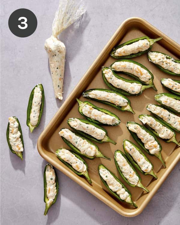 Jalapeno halves being filled with cream cheese.