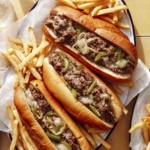 A platter of Philly Cheesesteak sandwiches with fries next to it.