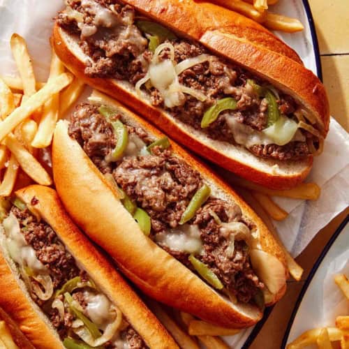 A platter of Philly Cheesesteak sandwiches with fries next to it.