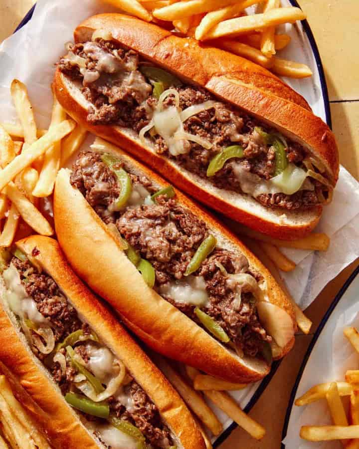 A platter of Philly Cheesesteak sandwiches with fries next to it.