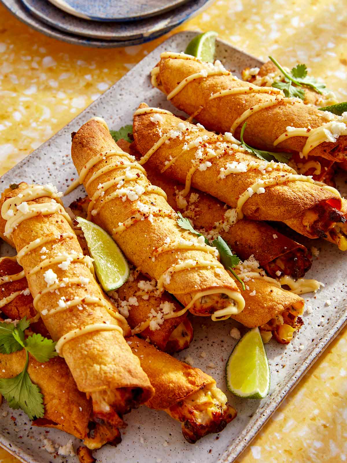 Taquitos on a platter with plates in the background.