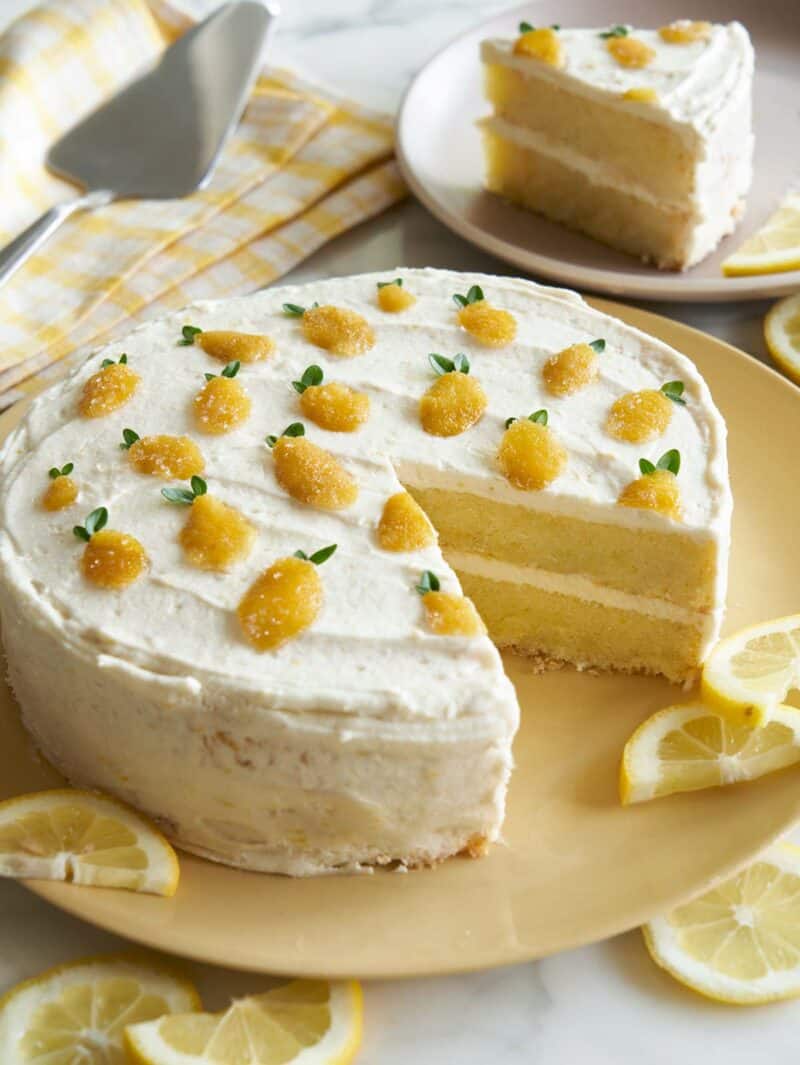 A lemon thyme layer cake with a piece cut out on a plate and lemon slices.