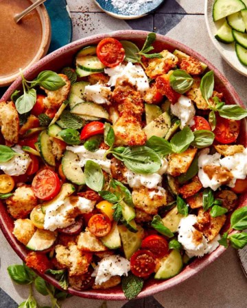 Panzanella salad in a bowl with fresh herbs next to it.