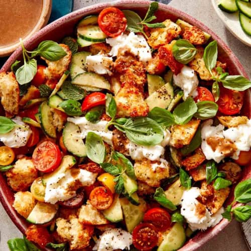 Panzanella salad in a bowl with fresh herbs next to it.
