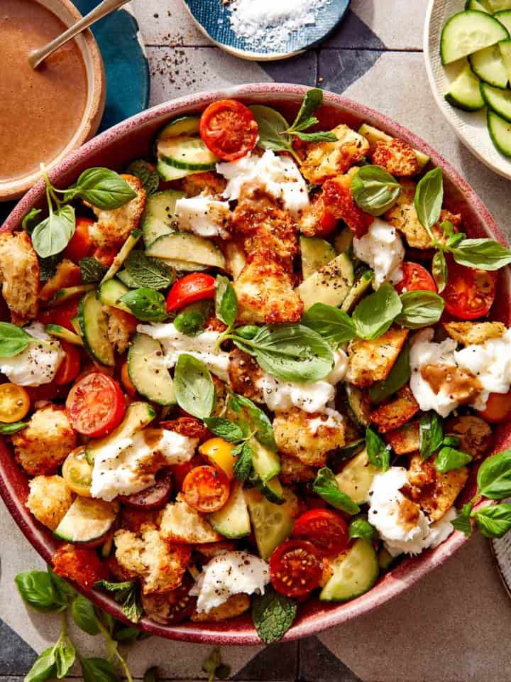 Panzanella salad in a bowl with fresh herbs next to it.