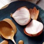 A spoon with balsamic vinaigrette on it resting on a plate with shallots next to it.
