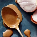 A spoon with balsamic vinaigrette on it resting on a plate with shallots next to it.