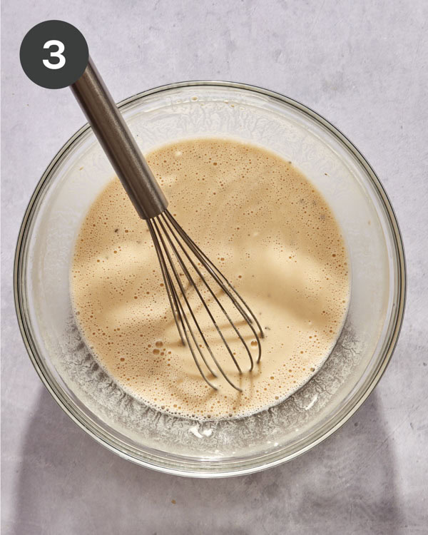 The batter to make beer battered fish in a glass bowl with a whisk in it.