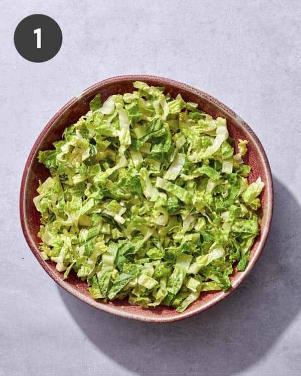Cobb salad lettuce in a bowl being tossed with dressing.