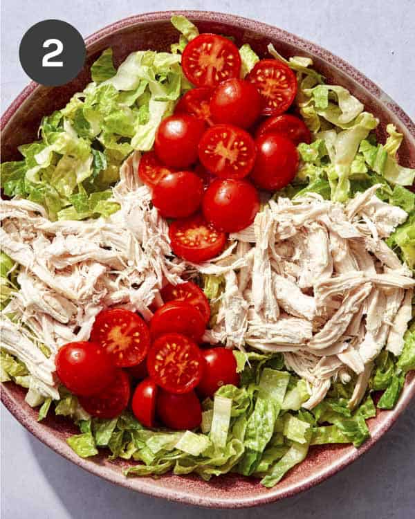 Cobb salad in a bowl with chicken and tomatoes on top.