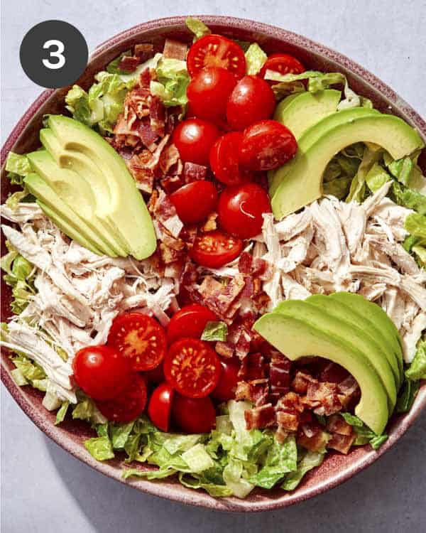 Cobb salad in a bowl with some toppings placed on the lettuce.
