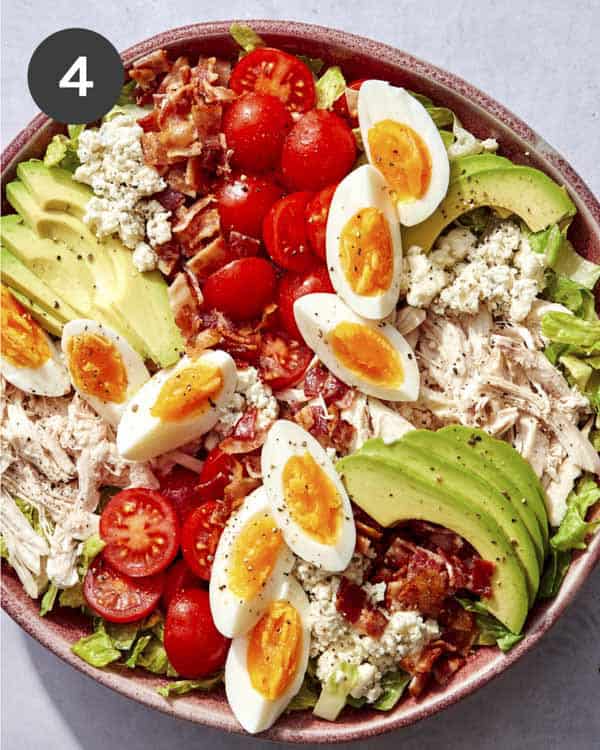 Cobb salad in a bowl with ingredients layered on top.
